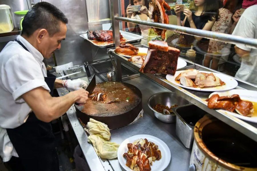 A chef skillfully chopping roasted meats at a popular hawker stall in Singapore