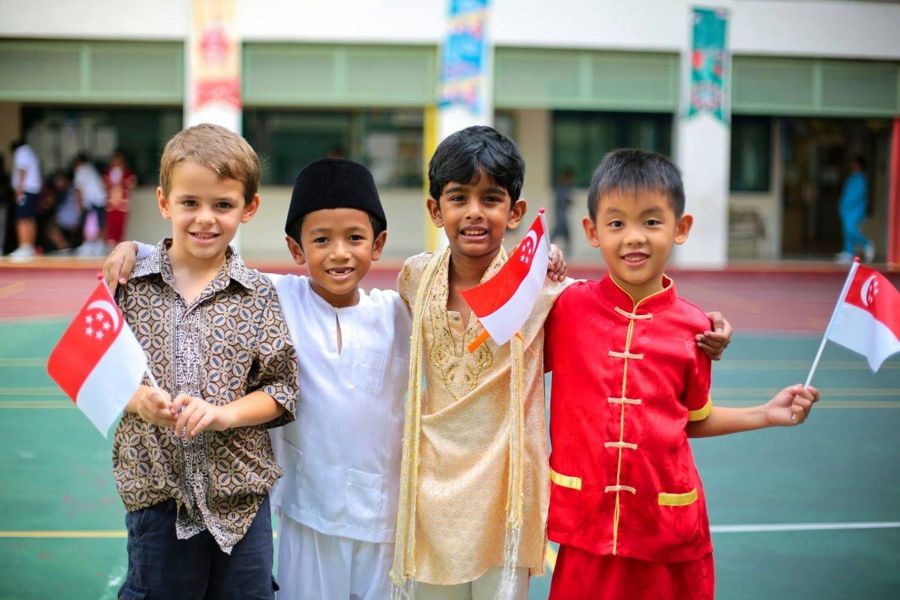 A group of children from different ethnic backgrounds dressed in traditional clothing, holding Singapore flags and celebrating Racial Harmony Day or National Day in Singapore
